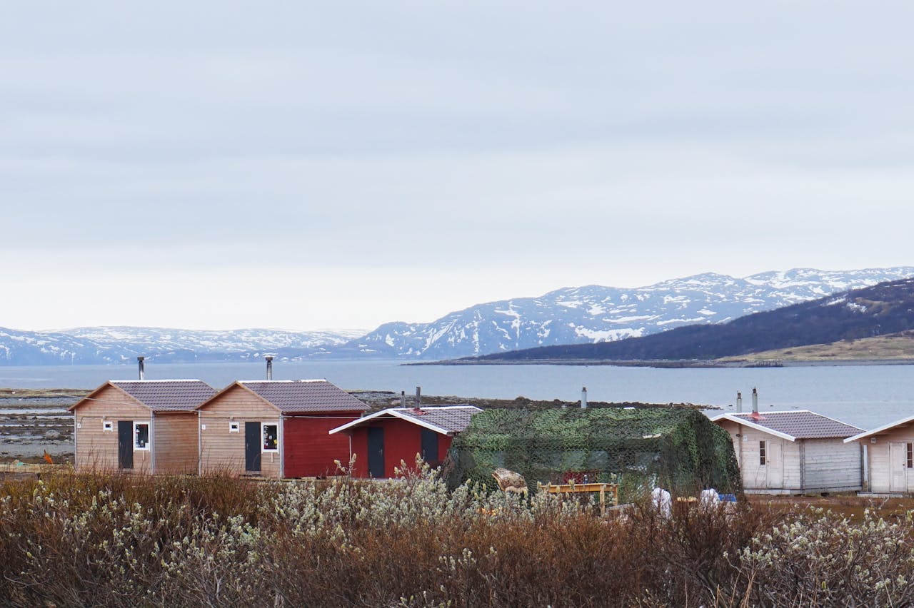 Charming wooden cabins near a serene Nordic waterfront with mountainous backdrop.