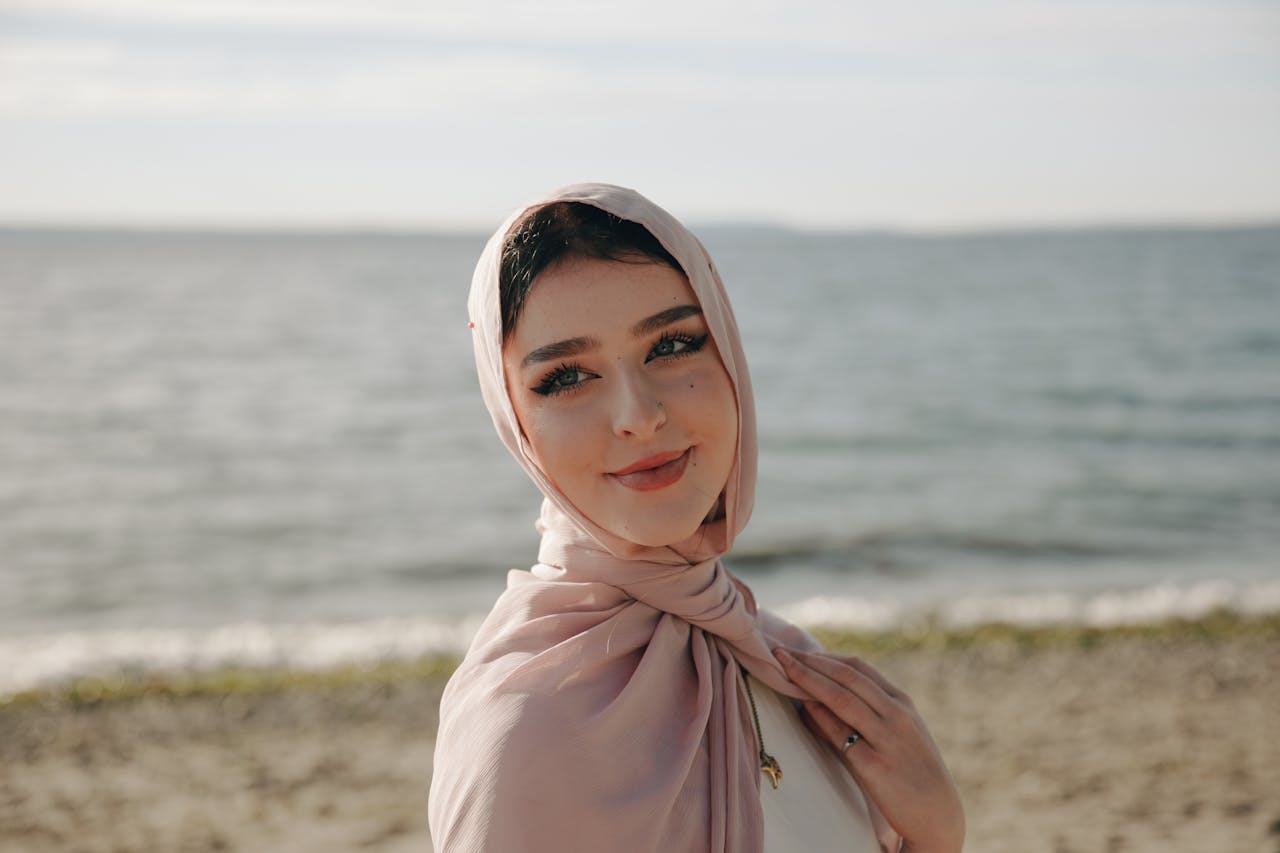 A serene portrait of a woman wearing a hijab, smiling by the seaside shore.